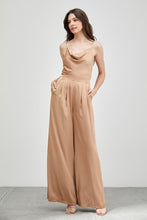 Load image into Gallery viewer, Our Above Status Satin Jumpsuit perfect blend of sophistication and texture that adds a touch of elegance to your wardrobe. This satin jumpsuit features a cowl neck design with intricate trim detailing, meticulously woven to create a unique and visually captivating ensemble.

