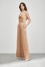 Load image into Gallery viewer, Our Above Status Satin Jumpsuit perfect blend of sophistication and texture that adds a touch of elegance to your wardrobe. This satin jumpsuit features a cowl neck design with intricate trim detailing, meticulously woven to create a unique and visually captivating ensemble.
