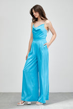 Load image into Gallery viewer, Our Above Status Satin Jumpsuit perfect blend of sophistication and texture that adds a touch of elegance to your wardrobe. This satin jumpsuit features a cowl neck design with intricate trim detailing, meticulously woven to create a unique and visually captivating ensemble.
