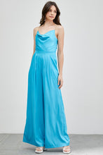 Load image into Gallery viewer, Our Above Status Satin Jumpsuit perfect blend of sophistication and texture that adds a touch of elegance to your wardrobe. This satin jumpsuit features a cowl neck design with intricate trim detailing, meticulously woven to create a unique and visually captivating ensemble.
